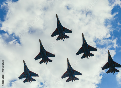 A squadron of jet soldiers, fighters, and airplanes perform a maneuver against the background of a blue and cloudy sky