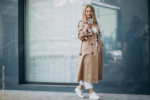 Fotografie Young woman in beige trench using phone outside