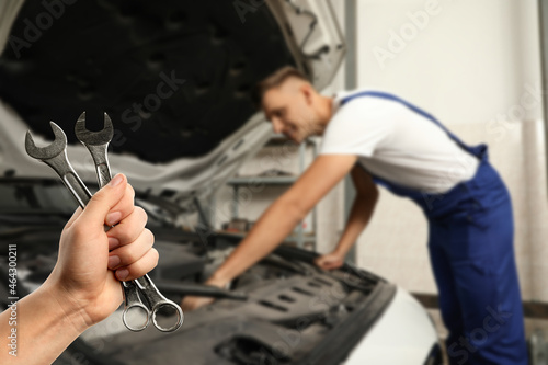 Auto mechanic with wrenches near broken down car in repair shop, closeup © New Africa