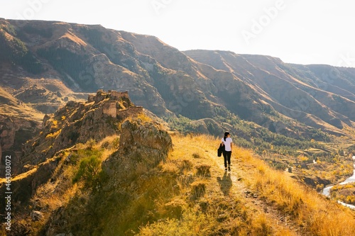 Female woman walks up the hill towards Tmogvi fortress surrounded by golden autumn nature and dramatic landscape in caucasus. Warm autumn golden colors nature outdoors