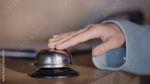 cropped view of woman pressing service bell on hotel reception counter.