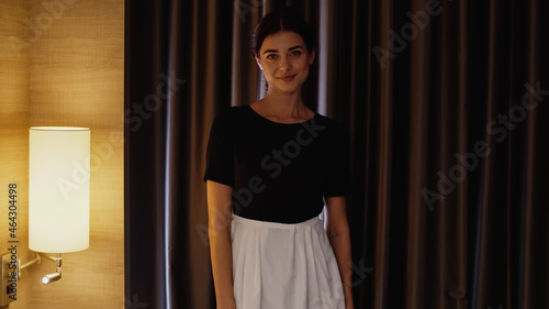 young maid in white apron smiling at camera in hotel room. © LIGHTFIELD STUDIOS