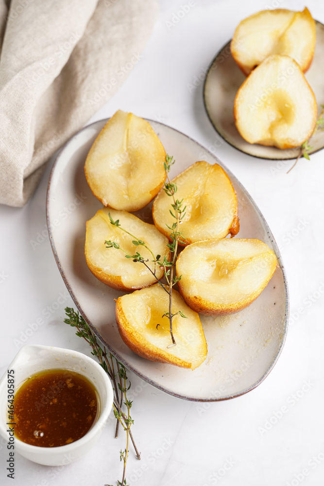 Caramelized pear halves on an oval grey plate with thyme branches and caramel on a white table surface, top view Caramelized pear halves on an oval grey plate with thyme branches and caramel on a white table surface, top view