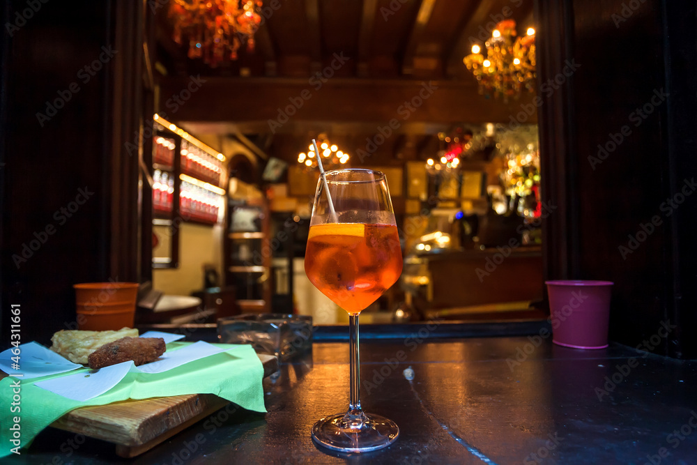 Wineglass with Aperol spritz on table of small bar. Old city restaurant with traditional refreshing alcohol drinks at evening time