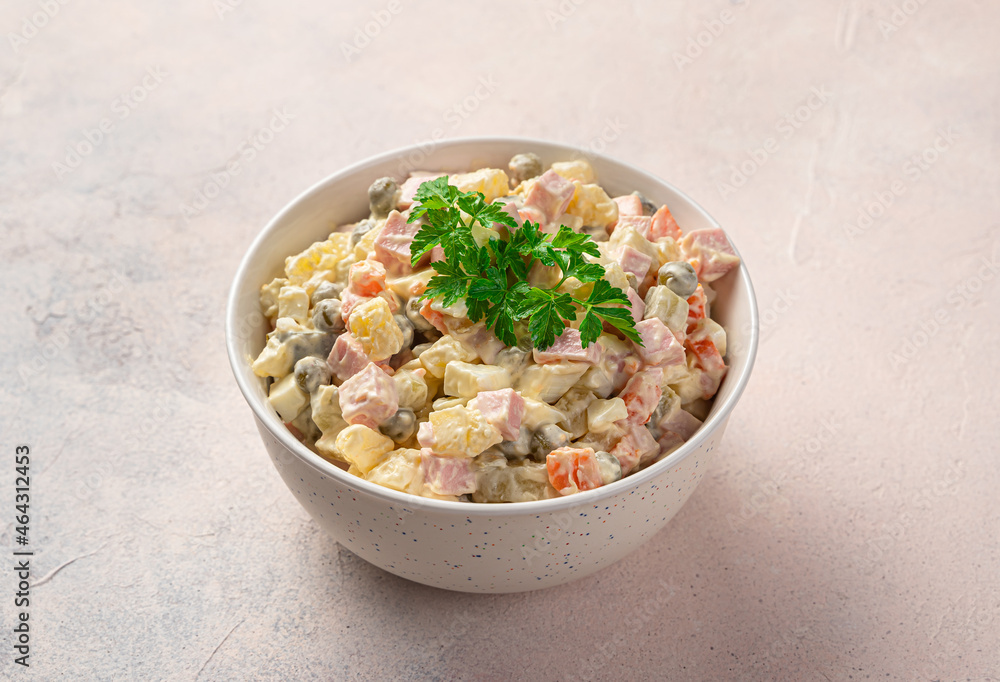 Olivier salad with vegetables, sausage and mayonnaise in a white bowl on a light pink background. Olivier salad with vegetables, sausage and mayonnaise in a white bowl on a light pink background.