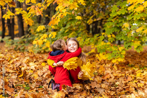 Happy children little girls cuddle in yellow maple leaves in autumn park outdoor