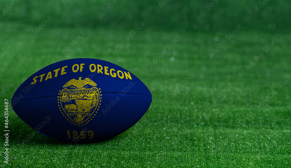 American football ball with Oregon flag on green grass background, close up American football ball with Oregon flag on green grass background, close up