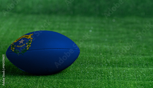 American football ball with Nevada flag on green grass background, close up
