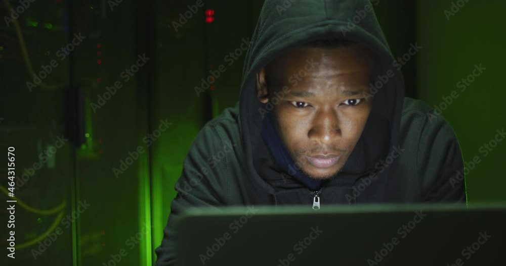 African american male computer hacker using laptop in business server room African american male computer hacker using laptop in business server room