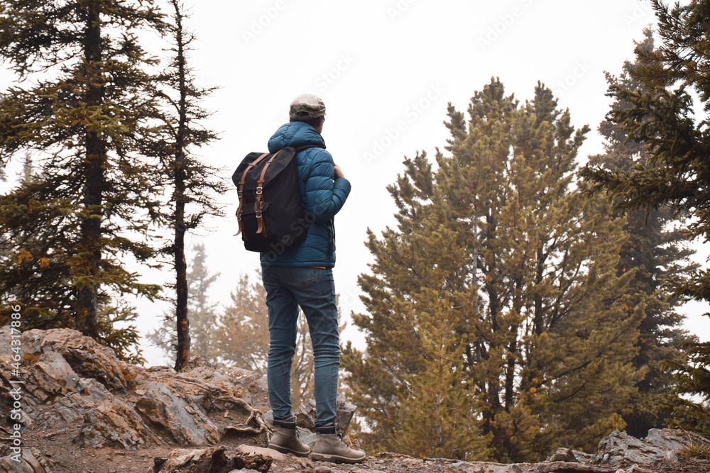 Woman with backpack standing on mountain trail looking into the foggy distance