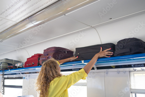 Quadro su tela Businesswoman taking bag from luggage compartment in train