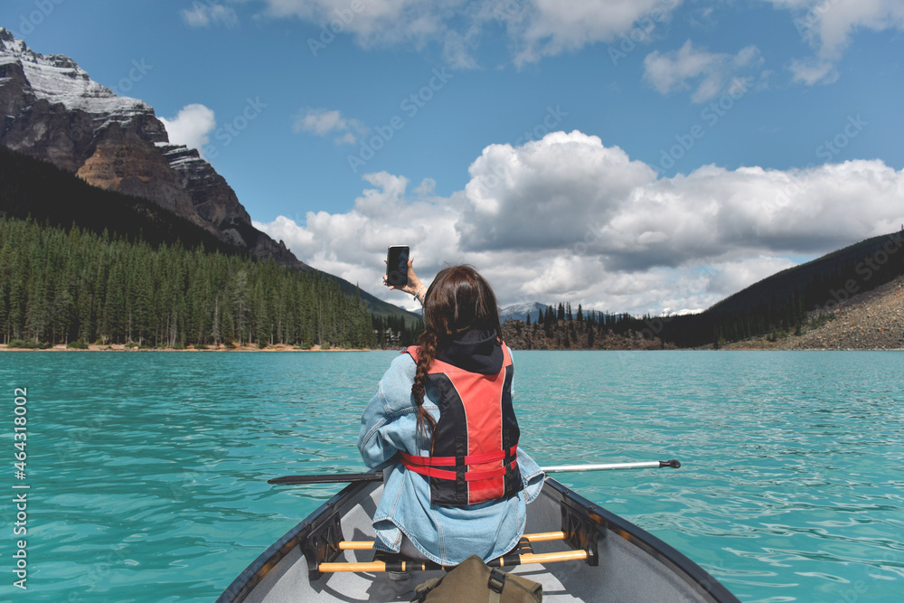 Young girl taking selfie while paddling in a canoe on turquoise lake surrounded by mountains Young girl taking selfie while paddling in a canoe on turquoise lake surrounded by mountains