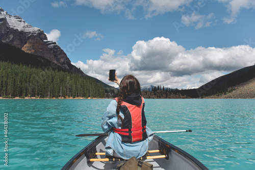 Young girl taking selfie while paddling in a canoe on turquoise lake surrounded by mountains