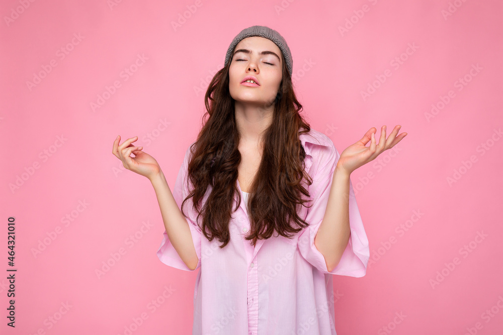 Attractive concentrated calm cute nice adorable tender young curly brunette woman wearing pink shirt and gray hat isolated on pink background with copy space. Yoga concept Attractive concentrated calm cute nice adorable tender young curly brunette woman wearing pink shirt and gray hat isolated on pink background with copy space. Yoga concept