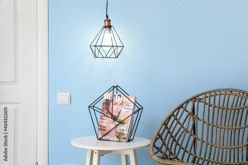 Glowing lamp and table with magazine near blue wall Glowing lamp and table with magazine near blue wall