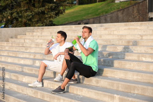Sporty young men drinking water on stairs outdoors