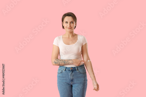 Young woman pointing at plaster onto her arm on pink background © Pixel-Shot