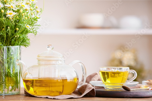 Teapot and cup of natural chamomile tea with flowers on table