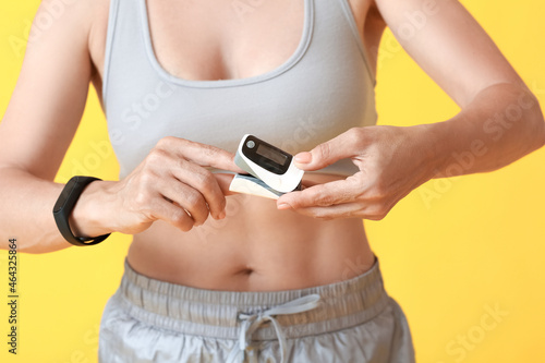 Female runner with pulse oximeter on color background, closeup photo