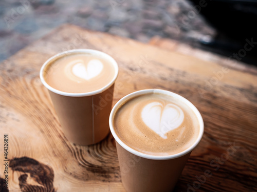 Cappuccino coffee in cardboard mug on wooden table at outdoor cafe