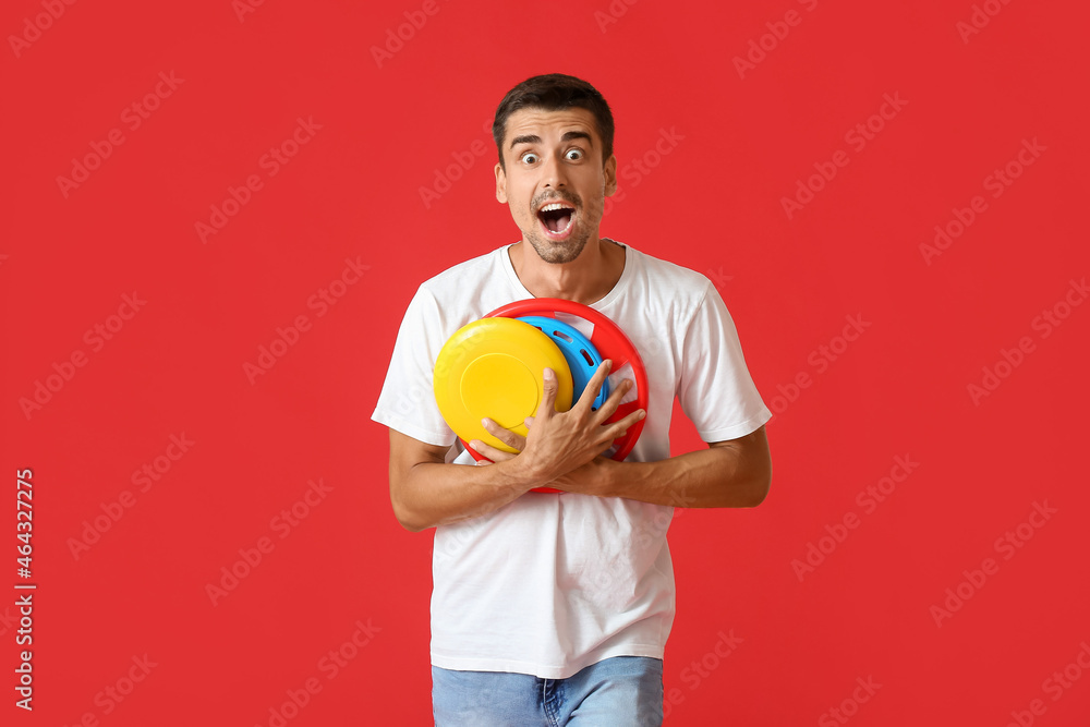 Surprised young man with frisbee on red background