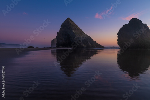 Majestic seascape Two rocks in the ocean reflected in the water. The sky is colored by the orange rays of the setting sun. Twilight. The beauty of nature, romance, tourism, relaxation, quiet scenes.