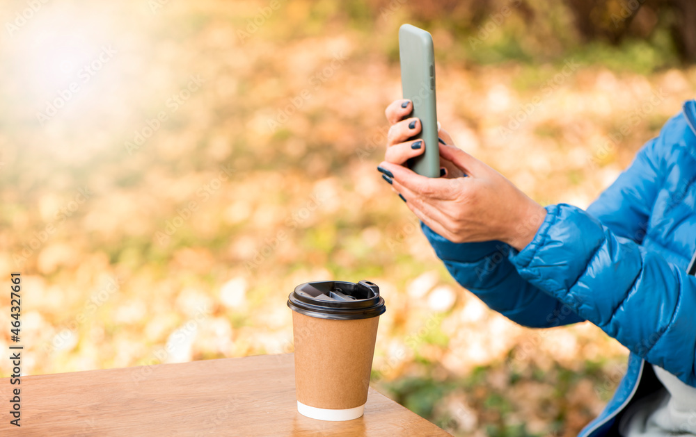 Close-up of a girl's hand makes a photo of coffee from a smartphone for instagram, social networks on an autumn background Close-up of a girl's hand makes a photo of coffee from a smartphone for instagram, social networks on an autumn background