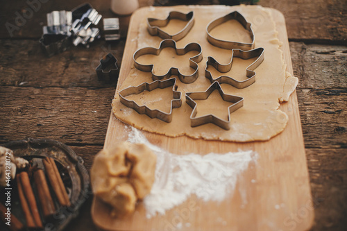Gingerbread dough with christmas metal cutters on wooden board. Atmospheric Moody image. Making traditional christmas gingerbread cookies on rustic table with spices and decorations