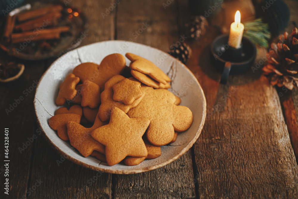 Freshly baked christmas gingerbread cookies in plate on background of rustic table with candle, spices, decorations. Moody image. Making traditional christmas gingerbread cookies. Happy Holidays Freshly baked christmas gingerbread cookies in plate on background of rustic table with candle, spices, decorations. Moody image. Making traditional christmas gingerbread cookies. Happy Holidays