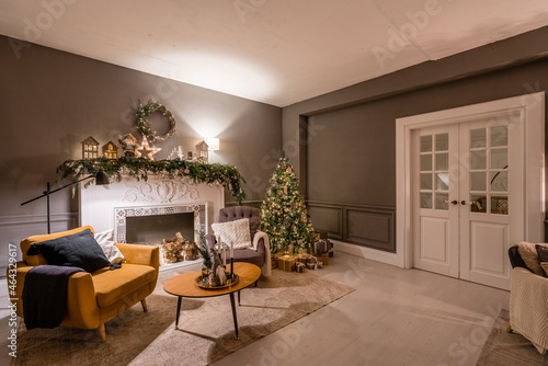 Classic apartments with decorated christmas tree and presents. Christmas evening in the light of candles and garlands. Living with fireplace and stucco. © malkovkosta