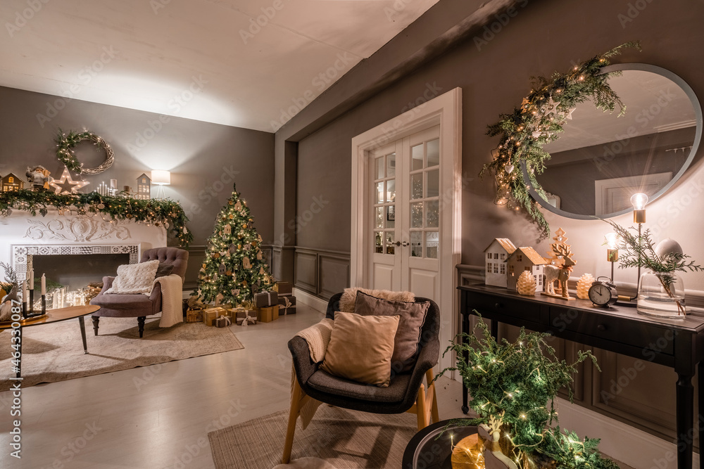 Fototapeta premium Classic apartments with decorated christmas tree and presents. Christmas evening in the light of candles and garlands. Living with fireplace and stucco.