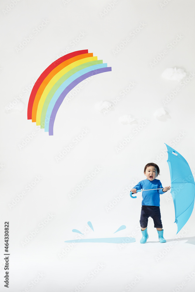 虹の下で水色の傘と水たまりで遊ぶ子ども 虹の下で水色の傘と水たまりで遊ぶ子ども