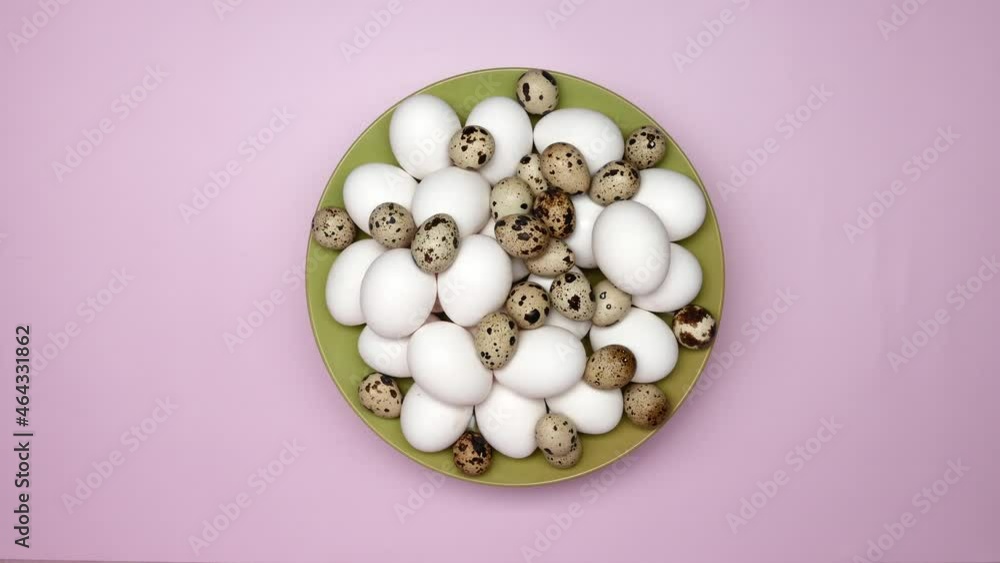Rotating White Chicken Eggs With Quail Eggs On A Green Plate On A Pink Background. Top View. Rotating White Chicken Eggs With Quail Eggs On A Green Plate On A Pink Background. Top View.