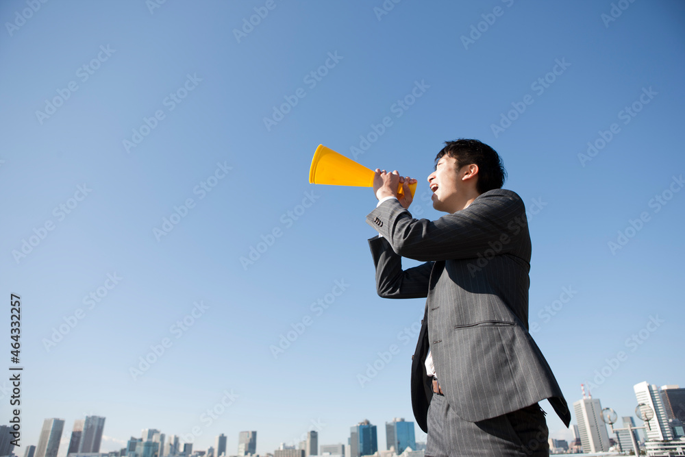 ビジネススーツを着て黄色のメガホンで叫んでいる男性