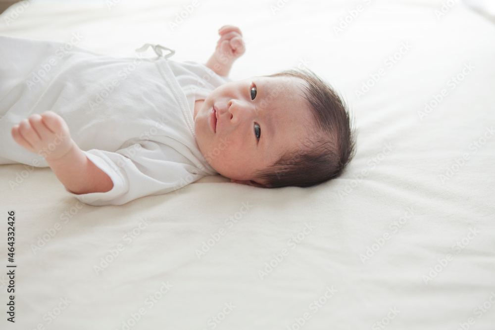 白い布団の上で横になってカメラを見つめる男の子の赤ちゃん 白い布団の上で横になってカメラを見つめる男の子の赤ちゃん