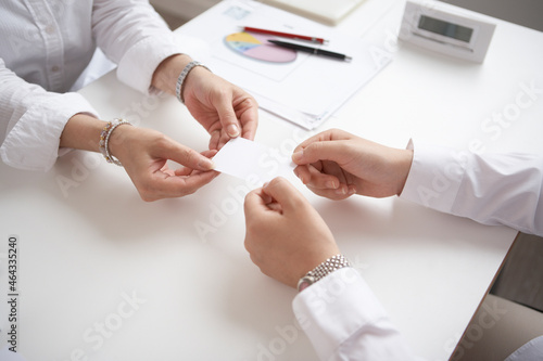 机の上で名刺交換をする2人の女性の手 photo
