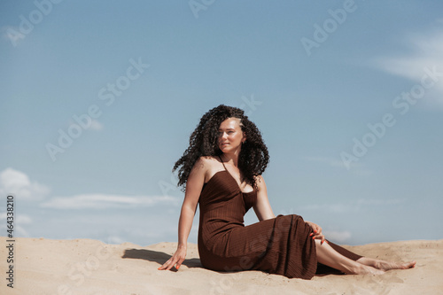 Dark brunette with voluminous curly hair among the Sands in a sand dune in a flying dress
