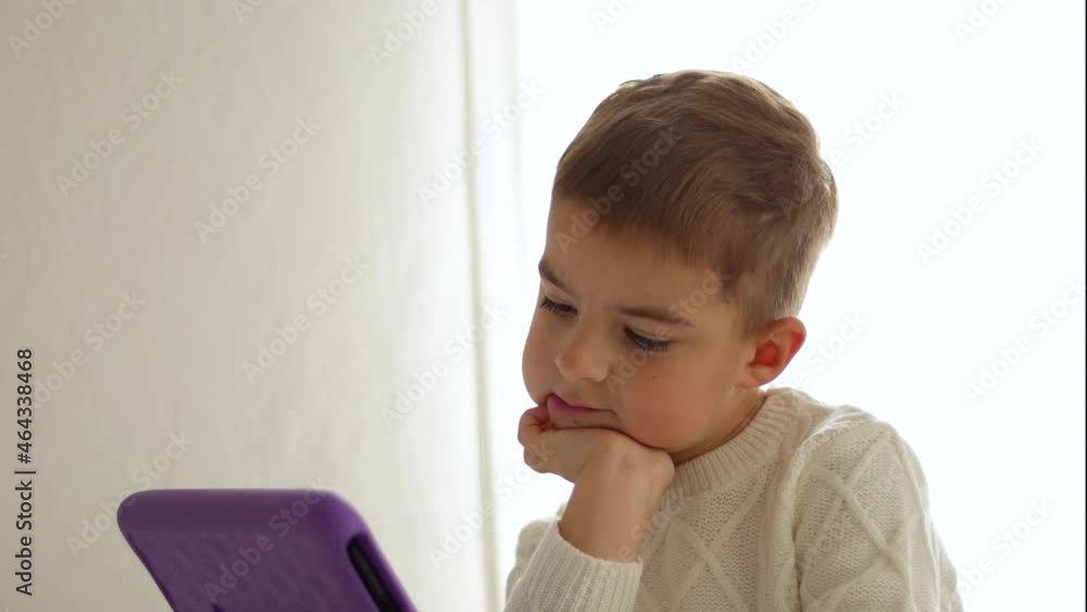 Happy little boy watching cartoon on digital tablet at home. Modern child and education technology. Happy little boy watching cartoon on digital tablet at home. Modern child and education technology.