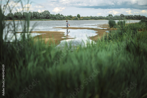 a boy with a net walks along the shore of a lake or river  in spring on flood  a landscape with a pond and a beautiful sky