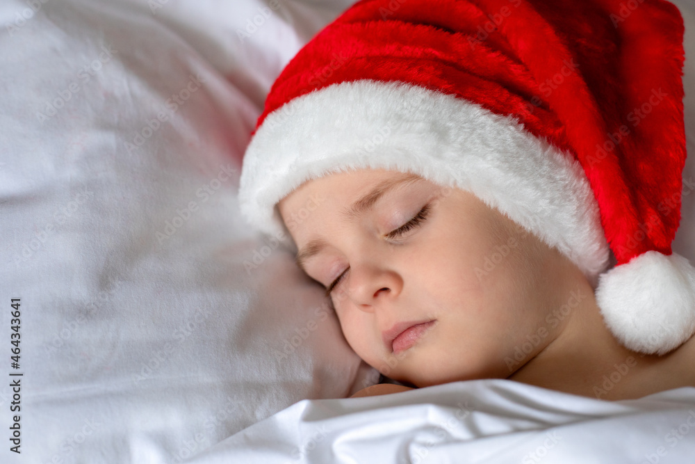A cute sleeping little boy in a red Christmas cap. Christmas atmosphere. A cute sleeping little boy in a red Christmas cap. Christmas atmosphere.