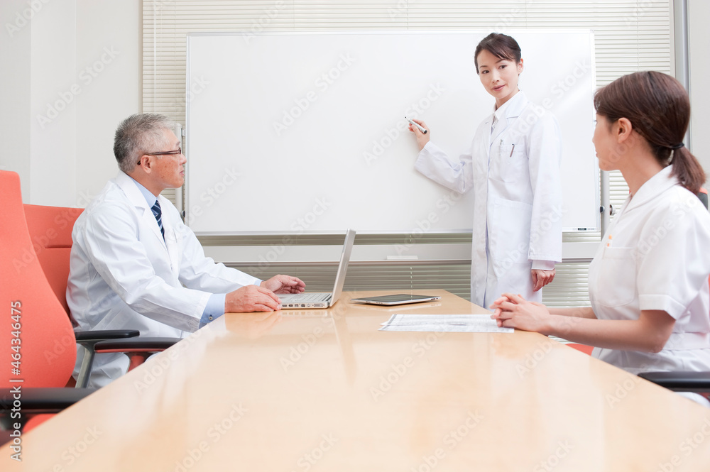 説明をする白衣を着た女医と説明を聞く医師と看護師 説明をする白衣を着た女医と説明を聞く医師と看護師