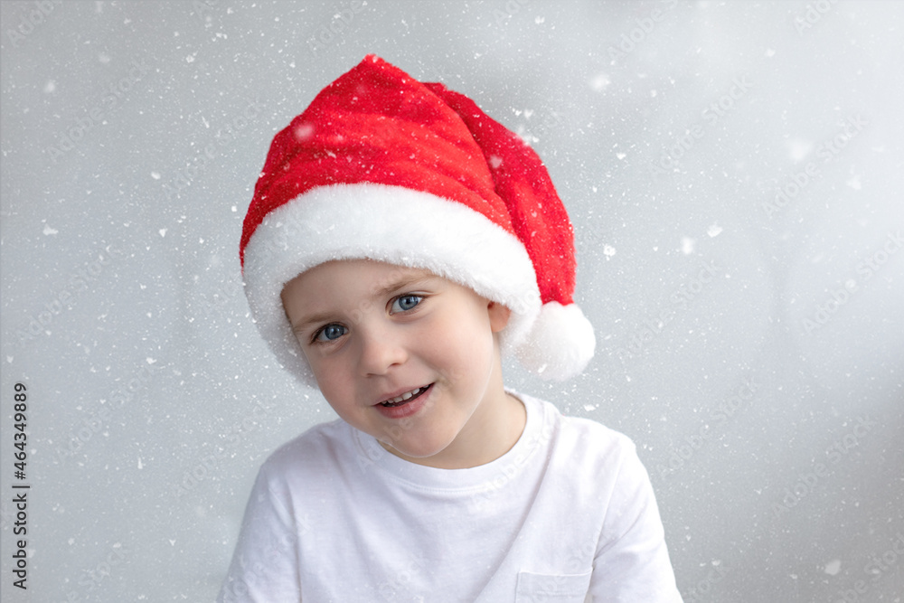 Cute smiling little boy in a Christmas red cap, he's happy. Light background with snow. Concept Christmas, New Years atmosphere. Cute smiling little boy in a Christmas red cap, he's happy. Light background with snow. Concept Christmas, New Years atmosphere.