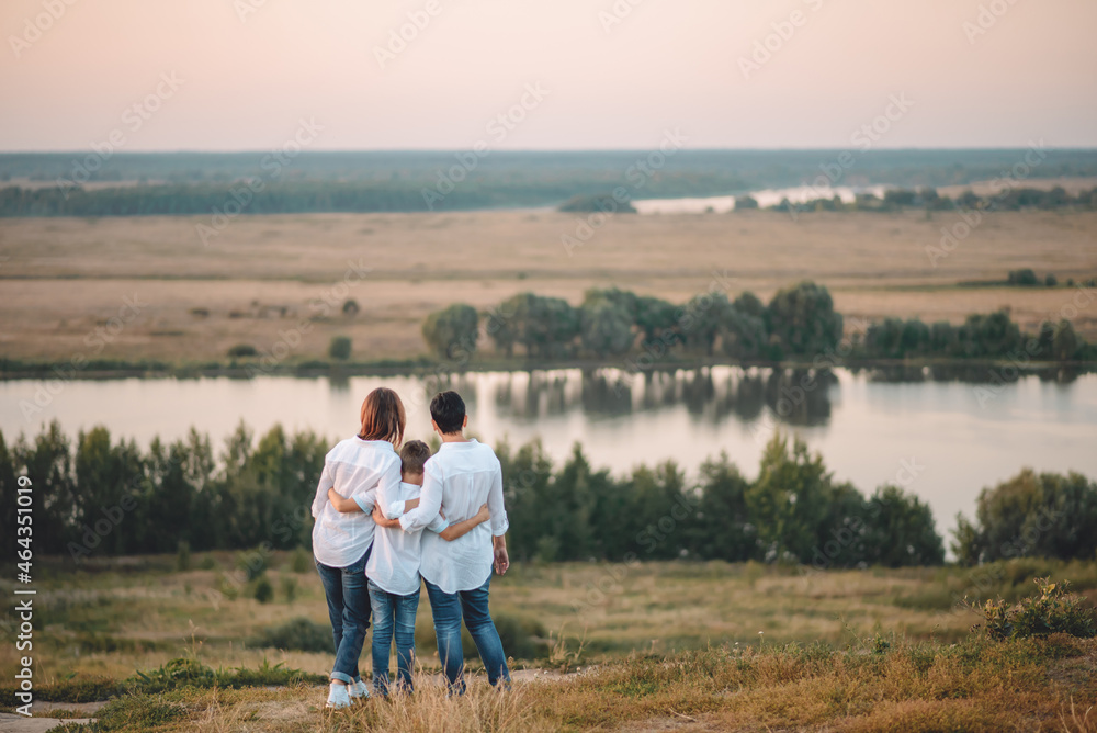 adults and a child are hugging each other on the riverbank and looking at the beautiful landscape