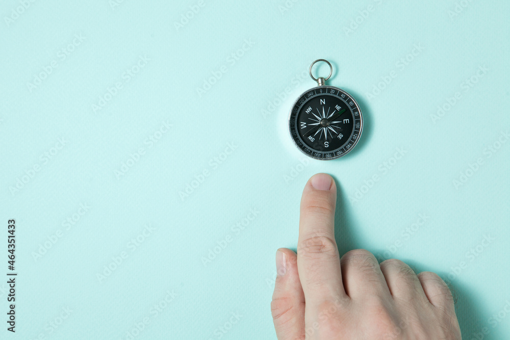 Compass on light blue background. The index finger points to the compass. Tool for travel, tourism, science, get lost, business and design and decoration. Flat lay design.