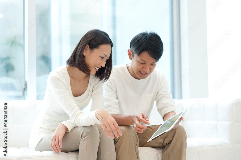 ソファに座ってタブレットPCを見る20代夫婦 ソファに座ってタブレットPCを見る20代夫婦