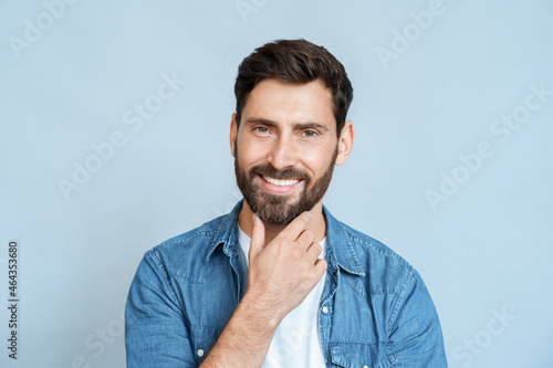 Portrait of caucasian man smiling and touching beard on face over blue wall