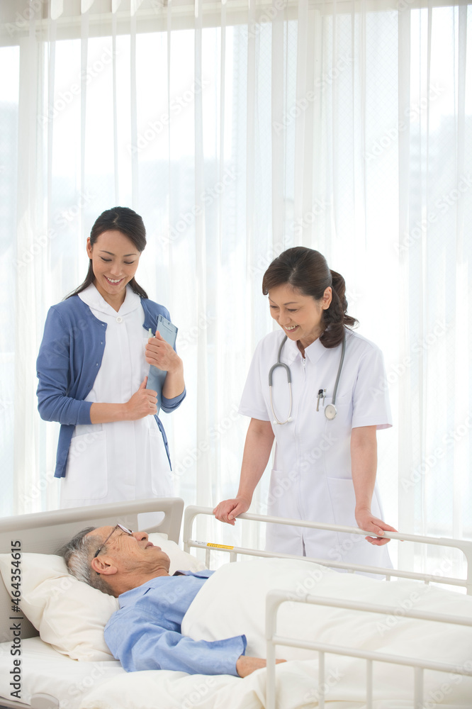 病院ベッドの老人を診察する女医と看護師 病院ベッドの老人を診察する女医と看護師