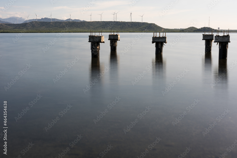 Dramatic long exposure image of piers in the Caribbean bay with wind turbines generating electricity in the background.