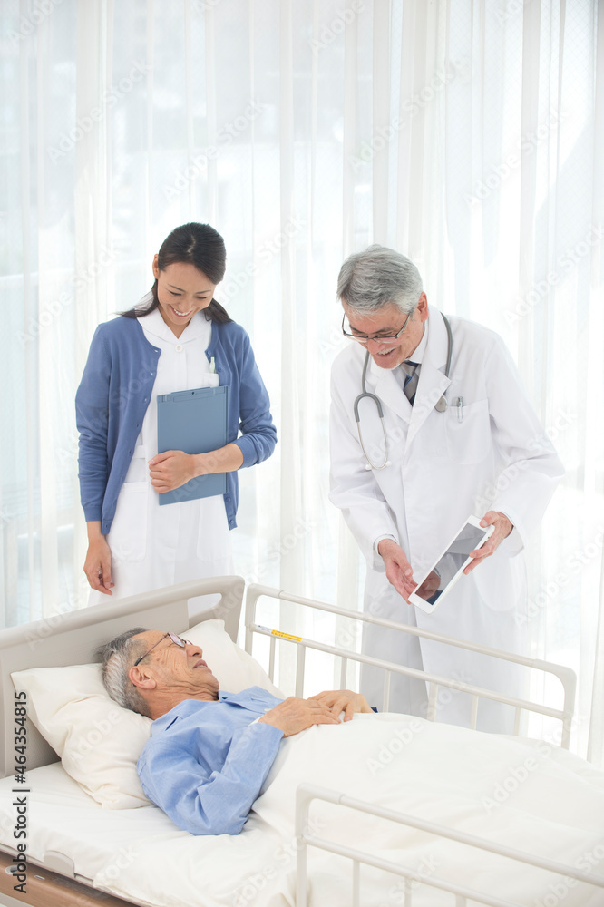 病院ベッドの老人を診察する女医と看護師 病院ベッドの老人を診察する女医と看護師