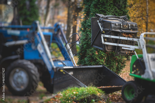 Removing fallen autumn leaves in the park, process of raking and cleaning the area from yellow leaves, regular seasonal work with tractor, garden tools and modern equipment